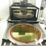 Silicon_wafers_on_machine,_detail_of_a_silicon_wafer_reflecting_different_colors.blurred_background